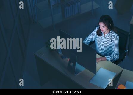 Young Thai Asian customer services care operators working night shift in call center for helping assistance client in workplace at night time Stock Photo