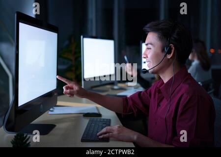 Young Thai Asian customer services care operators working night shift in call center for helping assistance client in workplace at night time Stock Photo