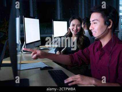 Young Thai Asian customer services care operators working night shift in call center for helping assistance client in workplace at night time Stock Photo