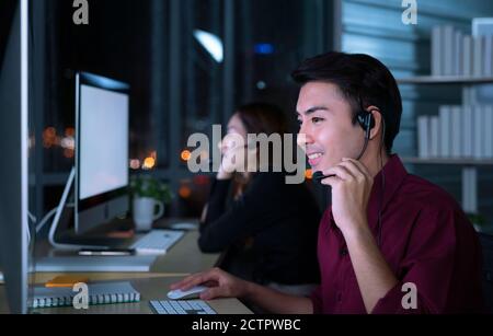 Young Thai Asian customer services care operators working night shift in call center for helping assistance client in workplace at night time Stock Photo