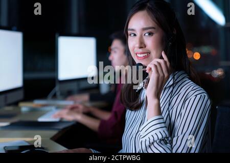 Young Thai Asian customer services care operators working night shift in call center for helping assistance client in workplace at night time Stock Photo