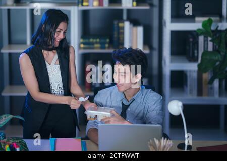 Businesspeople in the office at night working late, Two young businesspeople working overtime together takeout food Stock Photo