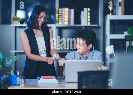 Businesspeople in the office at night working late, Two young businesspeople working overtime together takeout food Stock Photo