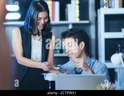 Businesspeople in the office at night working late, Two young businesspeople working overtime together takeout food Stock Photo