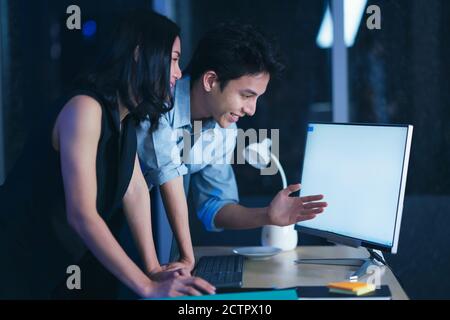 Businesspeople in the office at night working late, Two young businesspeople working overtime together over a laptop at a desk in an office in the lat Stock Photo