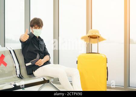 portrait of man traveler in protective mask holds passport during affected by flight delay and cancelled travel and vacation. Travel ban due to corona Stock Photo