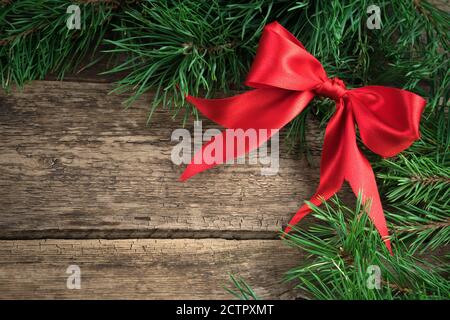 Red satin bow on pine branches on a natural wooden background. Stock Photo