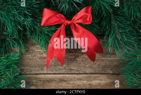 Christmas decorations made of red satin and fir branches of a bow on a natural wooden background. Stock Photo