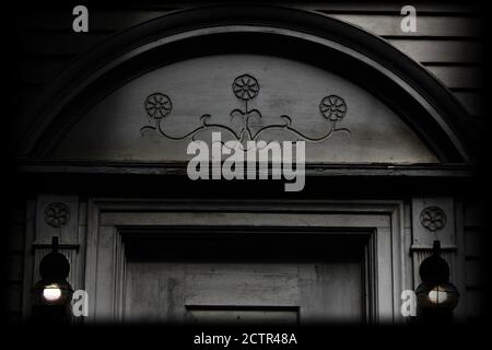 a pair of lamps illuminate the charming floral relief carving above an old door Stock Photo