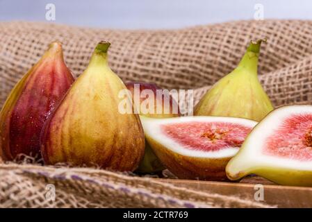 Fresh fig sliced in half with whole figs in the background, on a wooden surface. Fig fruits on a wooden platter. Stock Photo