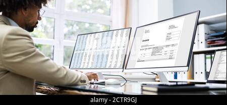 Looking At Invoice And Spreadsheet On Computer At Work Stock Photo