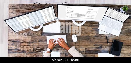 Looking At Invoice And Spreadsheet On Computer At Work Stock Photo