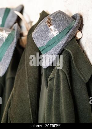 Traditional green hunter coat and grey hat with feather hanging on coat-rack. Hunting concept. Stock Photo