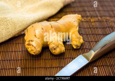 fresh ginger root on bamboo mat with knife and napkin, close-up Stock Photo