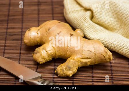 fresh ginger root on bamboo mat with knife and napkin, close-up Stock Photo
