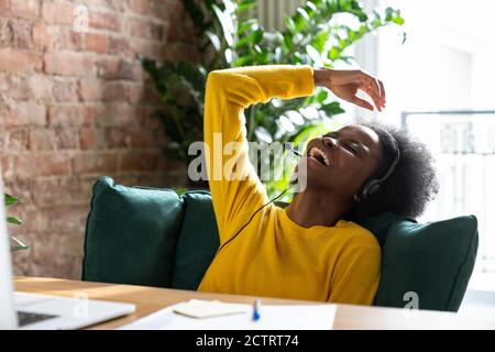 Smiling African American millennial woman wear headphones while talking to a client in video chat, teach online, watching webinar or video stream conf Stock Photo