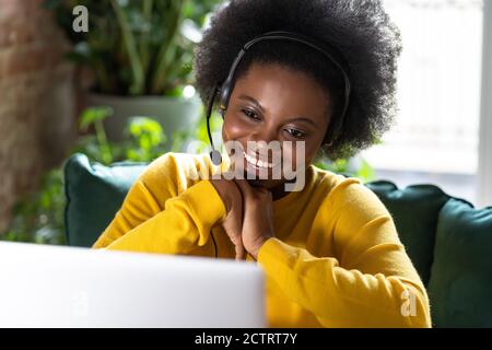 Smiling African American millennial woman wear headphones talk video calling, using laptop, teach online, communicating via zoom app, watching webinar Stock Photo
