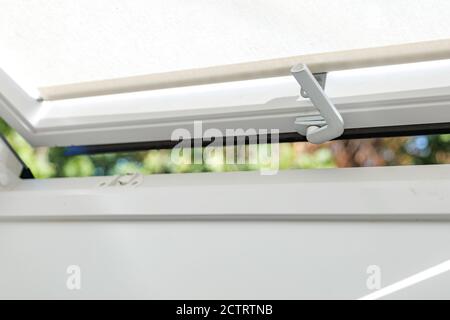 Close up view at slightly opening white Tilt Window Skylights with curtain at attic and defocused of outdoor green bokeh of tree. Stock Photo