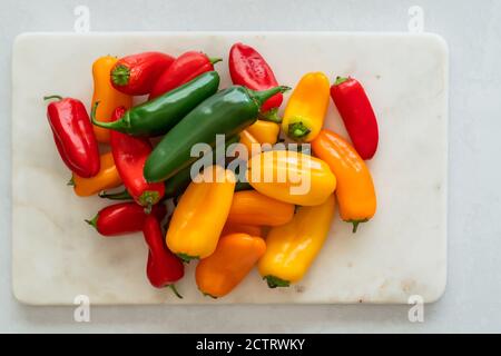 Fresh peppers assortment. Red pepper, yellow pepper, and jalapeno peppers close up on marble cutting board directly from above Stock Photo