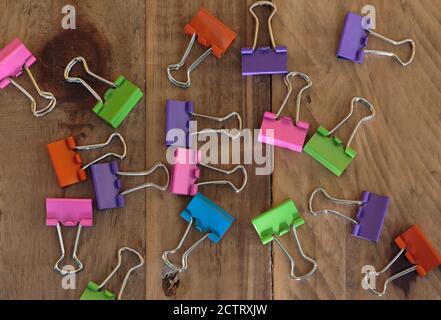 assorted binder clips in bright orange, pink, green, purple and blue colors scattered on a wood background Stock Photo