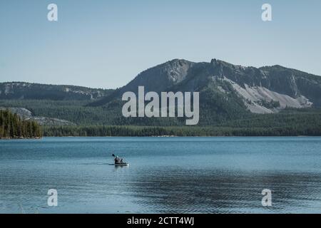 Pretty blue color reflecting off water mid afternoon on Paulina lake shore in high mountain cascades of central oregon with people on kayak. Stock Photo