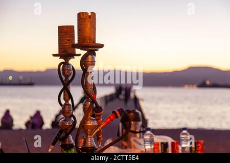 Close up view of two sets of hookah apparatus, a middle eastern tool to vape tobacco. In the background there is sunset over gulf of Aqaba, red sea. Stock Photo