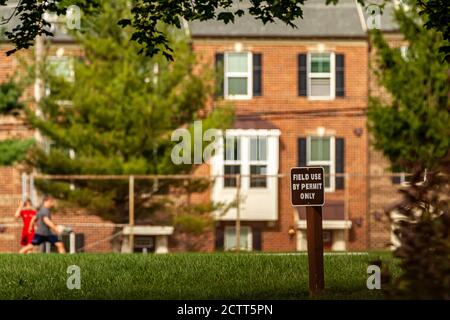 A selective focus image of a wooden sign post on a field that says 'field use by permit only' Kids living in neighboring houses are seen in blurred ba Stock Photo