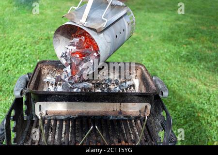 close up image of charcoal chimney starter filled with red glowing charred coal pieces. The chimney is lifted up from its handle and red hut burning c Stock Photo