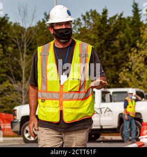 Bethesda, MD, USA 09/15/2020: A caucasian construction worker wearing safety equipment such as goggles, helmet and reflective vest is walking in const Stock Photo