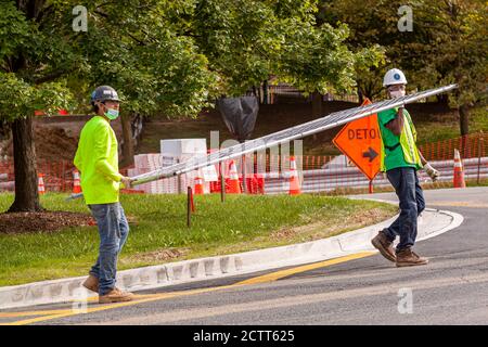 Bethesda, MD, USA 09/15/2020: A caucasian and an African American construction workers are carrying a metal wire fence panel in a construction site. T Stock Photo