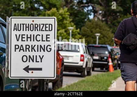 A white metal road sign saying 'Authorized vehicle parking only'. There is a long line of parallel parked cars by the sign post. A pedestrian man is w Stock Photo