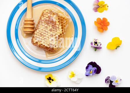 Honeycomb on a cornishware plate with a drizzler and edible flowers Stock Photo