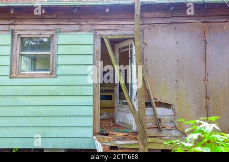 An abandoned very old house in the middle of woods . The one story building is poorly maintained with wooden frame rotting. The door is broken and the Stock Photo