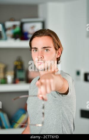 Serious looking handsome young man looking and pointing at the camera on an out of focus background. Stock Photo