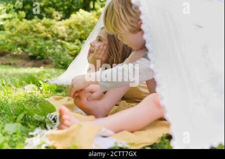 Girl (6-7) and boy (4-5) relaxing in homemade tent in backyard Stock Photo