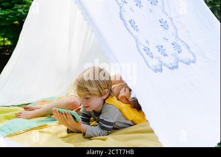 Girl (6-7) and boy (4-5) relaxing in homemade tent in backyard Stock Photo