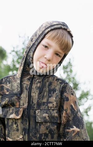 frustrated little boy in camouflage uniform shows tongue, upset at losing war game Stock Photo