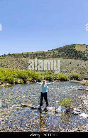 USA, Idaho, Sun Valley, Woman with arms raised standing on rocks in river Stock Photo