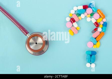 A question mark from laid out of medicine pills with stethoscope on blue background. Stock Photo