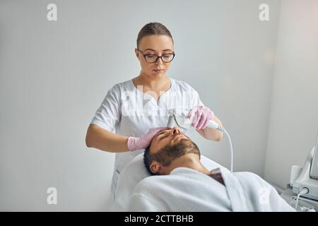 Female cosmetologist treating male skin with laser device Stock Photo