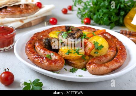 Tasty homemade grilled sausages with baked herb potatoes, mushrooms, cherry tomatoes and ketchup on a wooden background. Oktoberfest snack. Summer pic Stock Photo