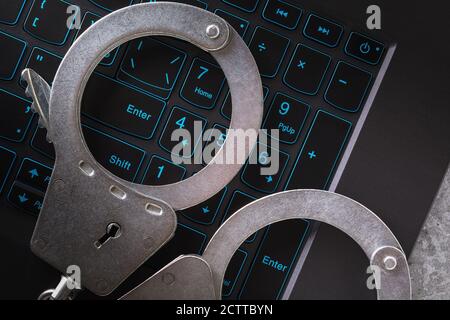 Handcuffs on a laptop keyboard, close-up. Concept on the topic of punishment for fraudulent activities in the digital space Stock Photo