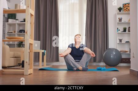 Senior woman relaxing in living room doing yoga. Active healthy lifestyle sporty old person training workout home wellness and indoor exercising Stock Photo