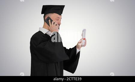 Graduating student walking and making a call on gradient backgro Stock Photo