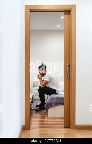 Hispanic man sitting on a bed and thinking Stock Photo