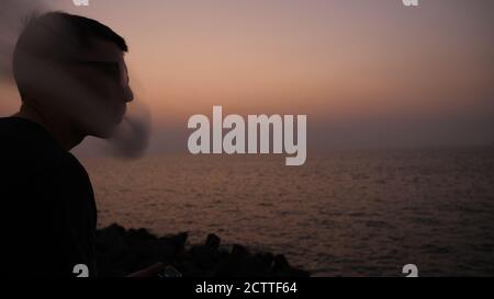 A guy at sunset smokes a e-cigarette. Vape. Vapping. Stock Photo