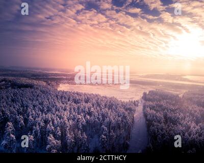 Toned. Village near field. Winter forest around. Cloudy sky and sun. Aerial view. Stock Photo