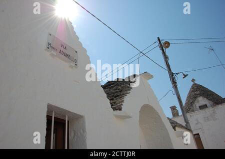 trulli houses angle view and street name sign on the façade and eletric wires between building. typical italian urban landscape Stock Photo