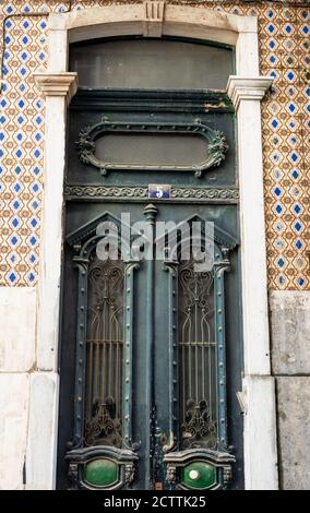 facade decorated with azulejos, hand-painted ceramic tiles, around green wooden door with wrought iron decorations.Lisbon, Portugal Stock Photo