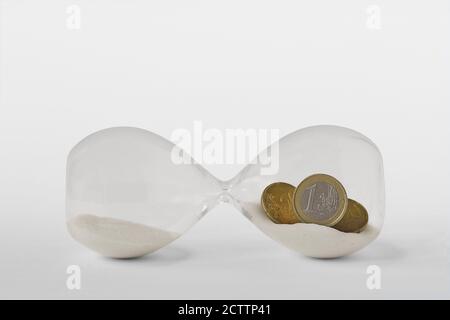 Hourglass with euro coins lying on white background - Concept of economy and stopping time Stock Photo